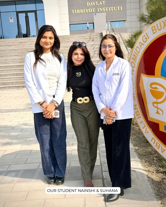 Nainshi and Suhana in white coats with a Scholars Abroad representative at the campus